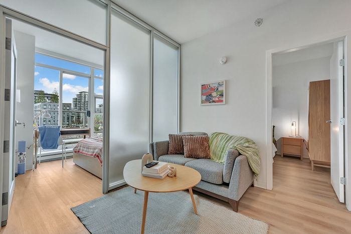 Bright and modern apartment living area with cozy sofa, stylish coffee table, and sliding glass doors opening to a bedroom. Abundant natural light highlights a serene, urban view.