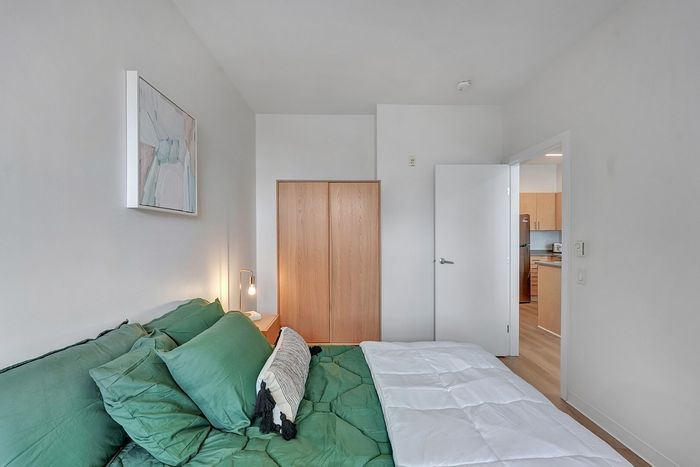 Inviting bedroom with modern decor, green bedding, soft lighting, and convenient kitchen access.