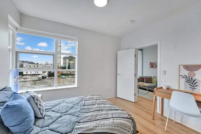 Bright apartment bedroom with large window view, cozy bedding, and access to a modern living room with stylish decor.