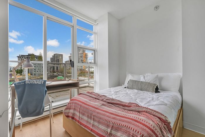Bright bedroom with floor-to-ceiling windows offering stunning city views, featuring a cozy bed and a stylish desk setup.