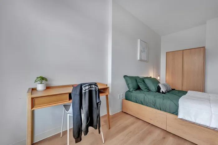 Modern bedroom with a stylish wooden desk, cozy green bed, and ample storage space, exuding a minimalist and inviting atmosphere.