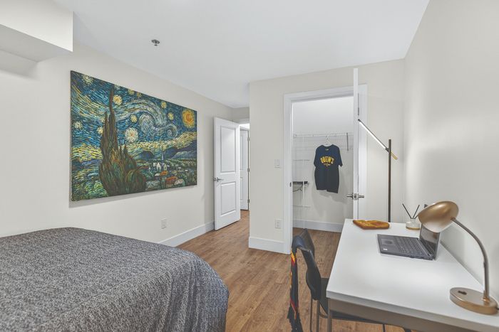 Modern bedroom with tasteful art piece, cozy bed, and study desk with sleek lighting. Spacious walk-in closet adds convenience.
