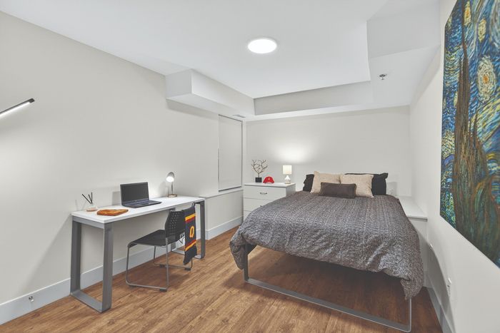 Modern bedroom with elegant decor, featuring a cozy bed, a sleek desk with a laptop, and stylish artwork on the wall.