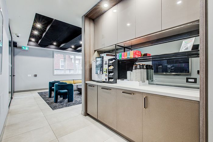 Modern apartment kitchen area with sleek cabinetry, a convenient coffee station, and stylish seating in an open-concept space.