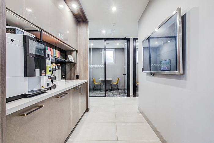 Modern office kitchen space with sleek cabinetry, a state-of-the-art coffee machine, and a nearby glass-walled meeting room.