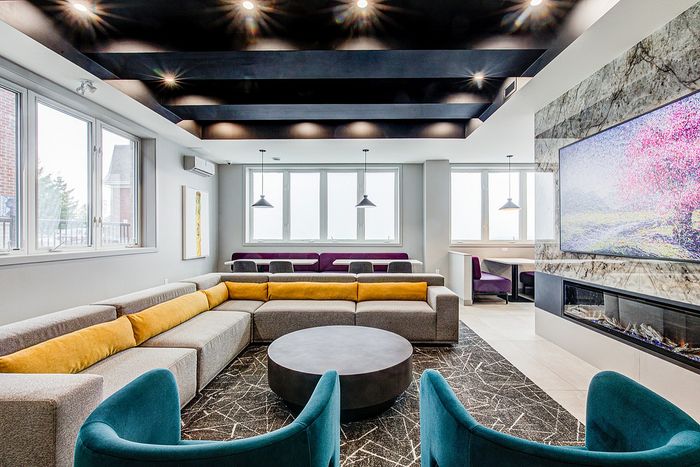 Modern luxurious living room featuring sleek gray and yellow sectional sofa, stylish blue chairs, large wall-mounted TV with scenic imagery, and ample natural light from expansive windows.