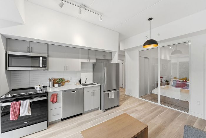 Modern kitchen design featuring sleek stainless steel appliances, abundant cabinet space, and a warm, open layout with a view into the cozy bedroom area.