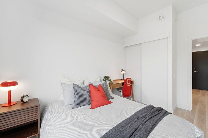 Modern bedroom with cozy bedding, vibrant red accents, sleek nightstand, and functional workspace.