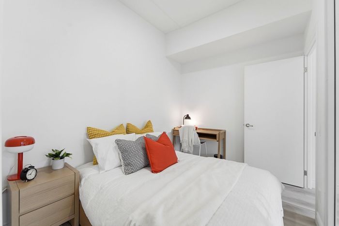 Bright, modern bedroom featuring a cozy bed with colorful pillows, sleek nightstand, and a functional desk area.