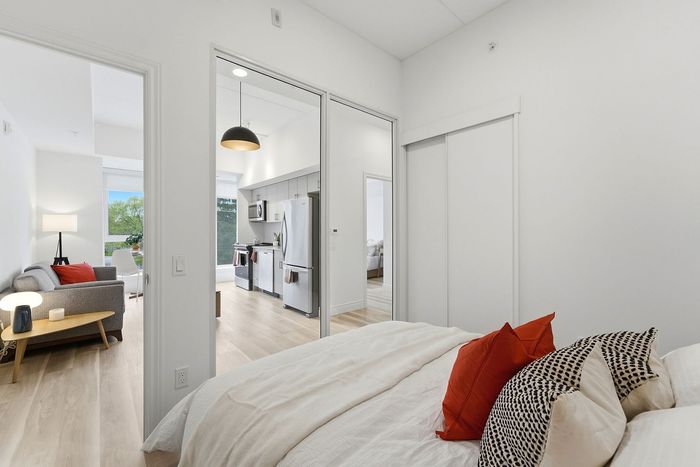 Modern open-concept apartment featuring a cozy bedroom with stylish red and patterned pillows, spacious living area, and sleek kitchen with stainless steel appliances.