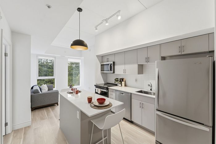 Contemporary kitchen and dining area with sleek stainless steel appliances, modern cabinetry, and cozy living space with large windows overlooking greenery.