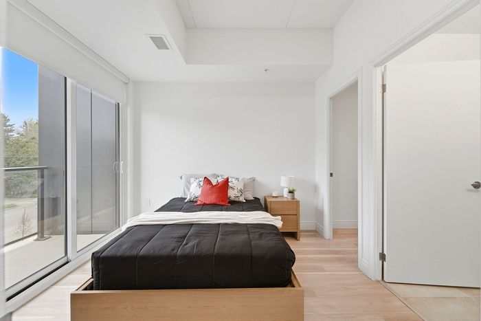 Bright modern bedroom with stylish black bedspread, vibrant red accent pillow, and large sliding glass doors opening to a serene view.