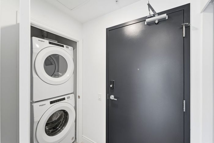 Modern apartment entryway featuring sleek black door and convenient in-unit washer and dryer setup.