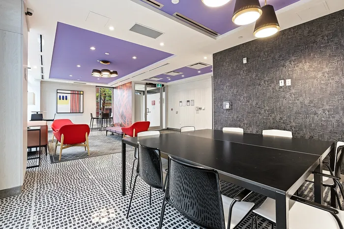 Modern communal lounge featuring vibrant red seating, sleek black dining table, and stylish overhead lighting on a striking purple ceiling.