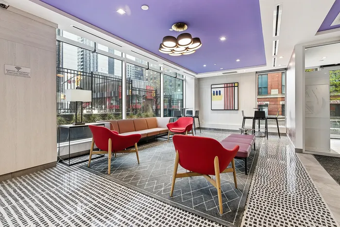 Modern apartment lounge with stylish red and brown seating, artistic wall decor, and a purple ceiling. Large windows provide natural light and a view of the cityscape.