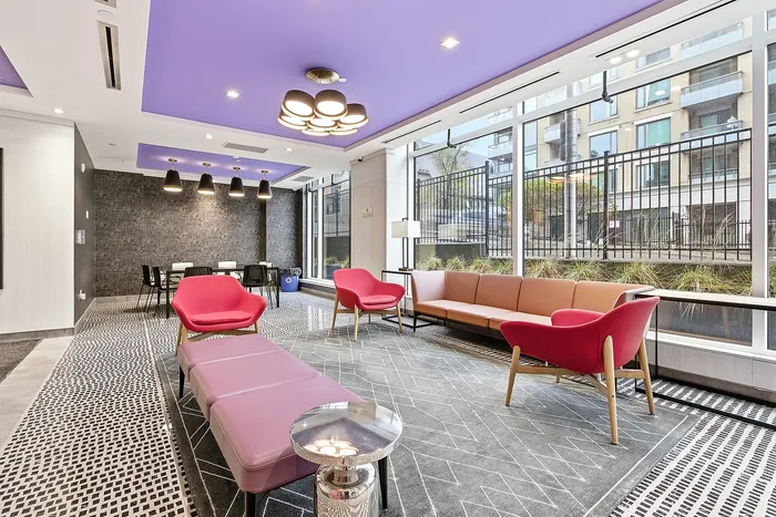 Stylish modern lounge area with vibrant purple ceiling, featuring chic red and pink seating, elegant lighting, and floor-to-ceiling windows offering an urban view.