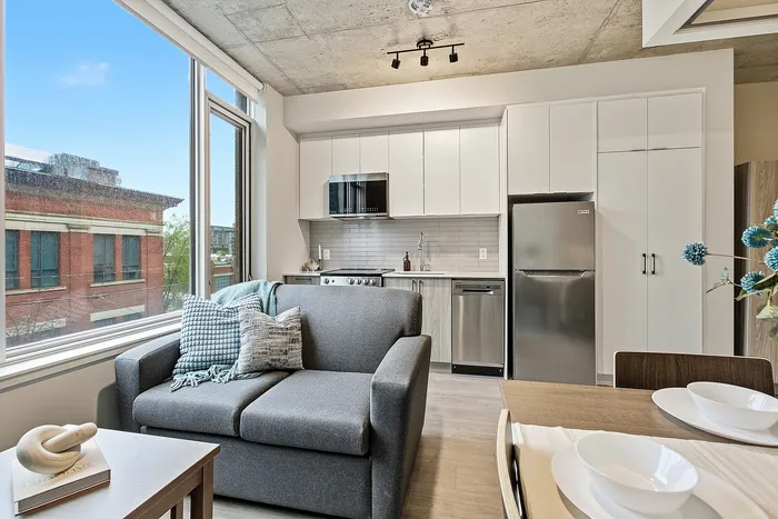 Chic urban apartment with a cozy living area, modern kitchen, and expansive city views through large windows.
