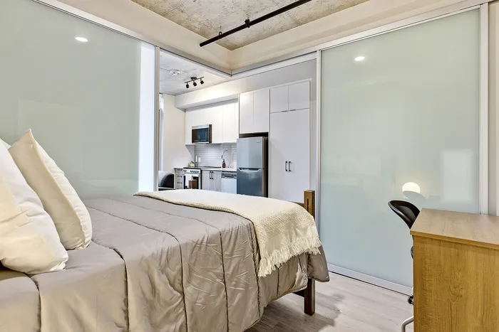 Modern studio apartment with a cozy bed, sleek kitchen, and stylish frosted glass sliding doors.