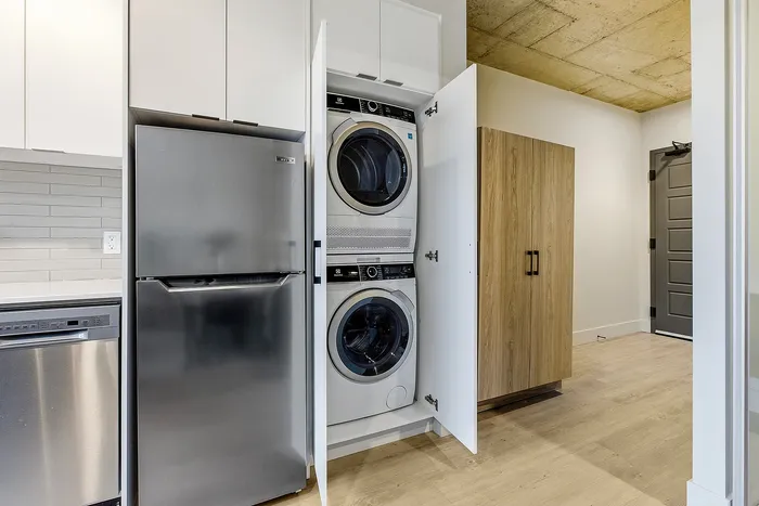 Modern apartment utility area with sleek stainless steel refrigerator, integrated washer and dryer, and stylish cabinetry.