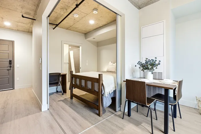 Modern studio apartment with a cozy bedroom nook, stylish open dining area, and sleek interiors under an industrial ceiling.