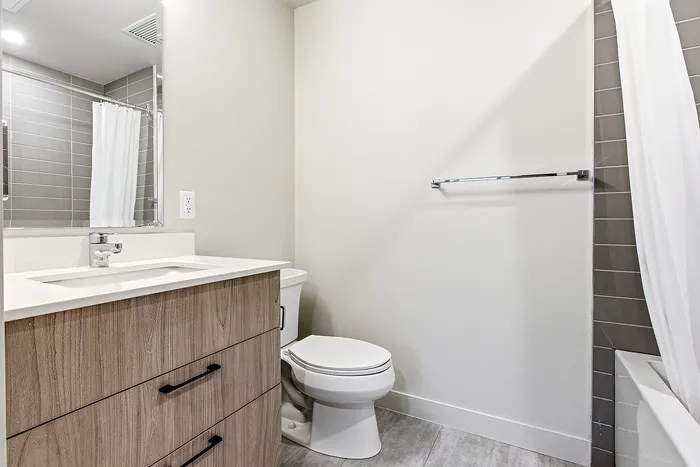 Elegant modern bathroom boasting sleek wood cabinetry, pristine white countertop, and a glossy tiled shower area.