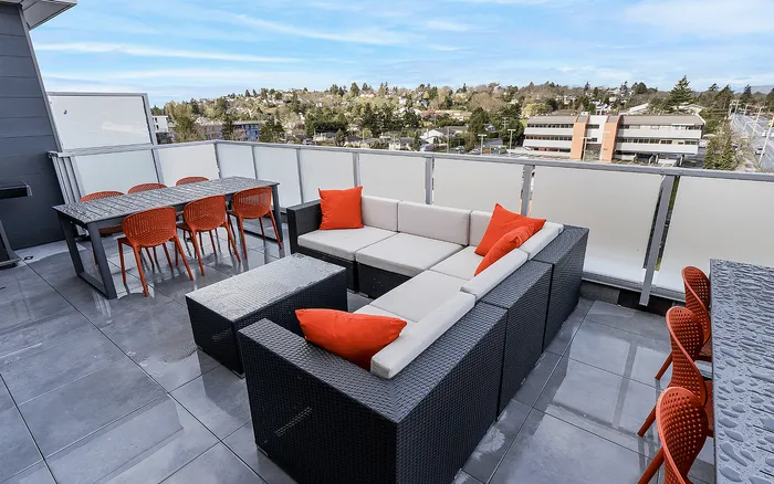 Modern rooftop terrace with wicker seating, vibrant red cushions, and a scenic city view; perfect for outdoor dining and entertaining.