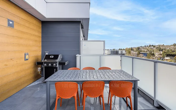 Chic rooftop patio with modern grill, vibrant orange chairs, and scenic views.