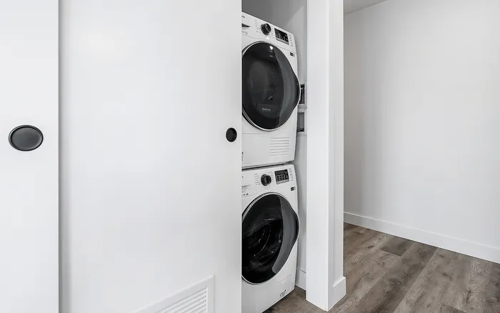 Modern apartment featuring a neatly tucked-in stackable washer and dryer unit in a sleek white closet, complemented by stylish wooden flooring.