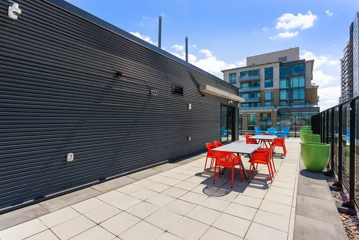 Contemporary rooftop patio with vibrant red chairs, sleek modern architecture, and cityscape view.