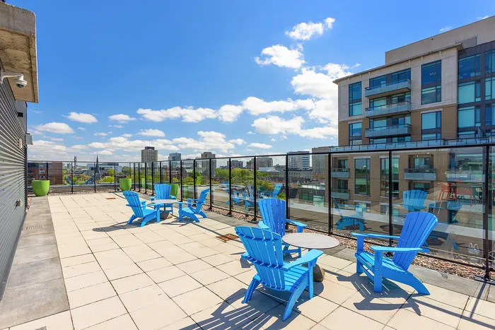 Sunny rooftop terrace with blue Adirondack chairs, offering stunning city views under a vibrant blue sky.