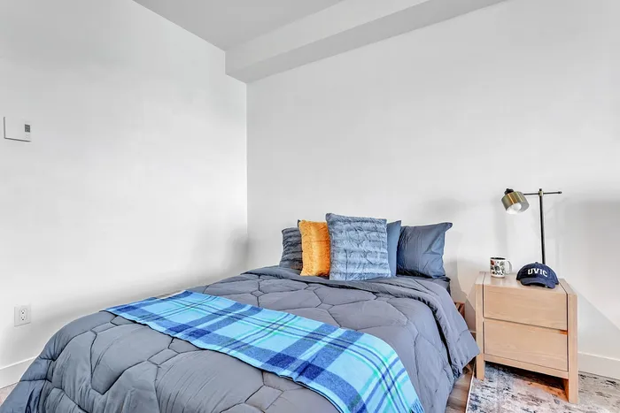Inviting bedroom with a cozy bed adorned with plush pillows and a stylish plaid throw, complemented by a modern bedside table and a sleek lamp.