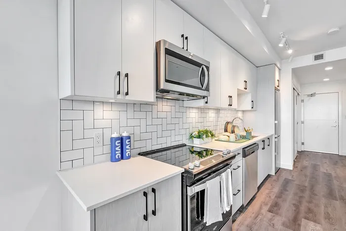 Modern kitchen with sleek white cabinetry, stainless steel appliances, and elegant tile backsplash on rich wood flooring.