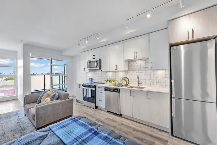 Modern open-concept kitchen and living area with sleek cabinetry, stainless steel appliances, and ample natural light from large windows.