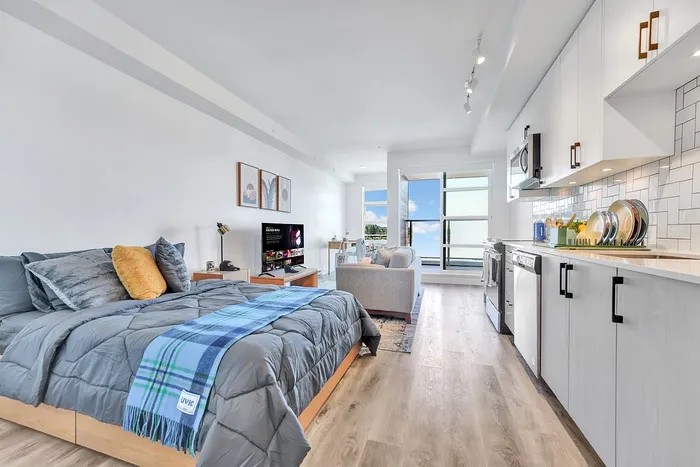 Modern studio apartment with cozy bed, stylish kitchen, and bright living area offering scenic views.