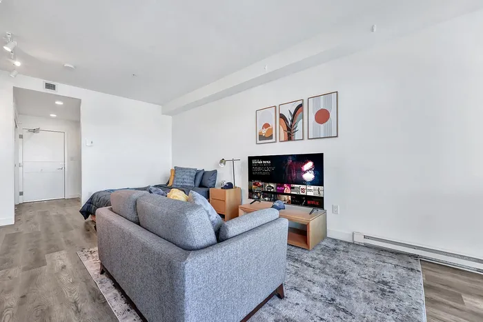 Modern living area with sleek wooden flooring, cozy gray couch, wall-mounted TV, and stylish abstract artwork creating an inviting atmosphere.