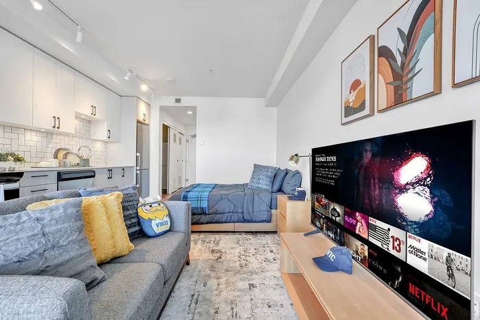 Modern studio apartment with sleek kitchen, cozy living space, and inviting decor featuring vibrant artwork and streaming entertainment on a large TV.