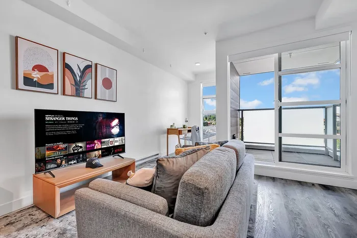 Bright and modern living room with stylish decor, large TV, cozy sofa, and access to a sunlit balcony with expansive views.