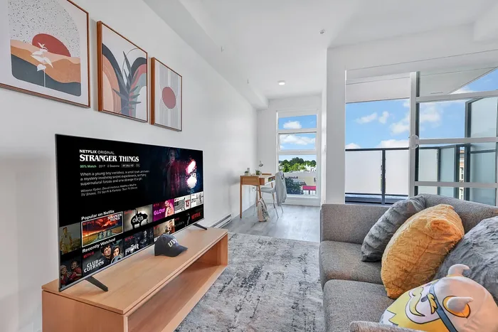Contemporary living room with plush sofa, large smart TV, artistic wall decor, and abundant natural light from balcony access.