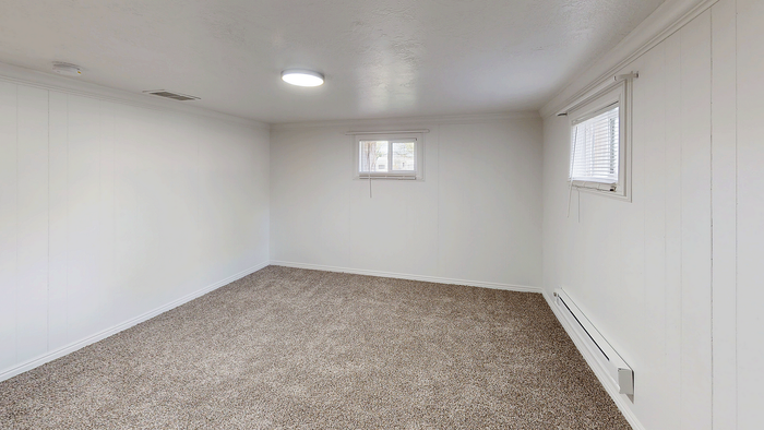 Basement bedroom with carpet flooring, natural light from two windows, and neutral paint at Stone Creek Village.