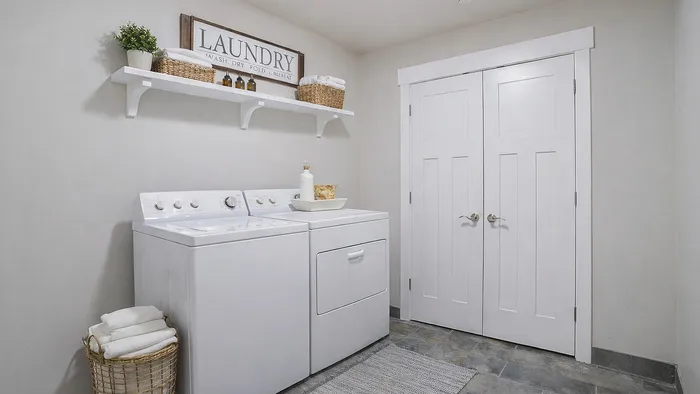 In-unit laundry room at Junction View Apartments featuring full-size washer and dryer with shelving and storage space.