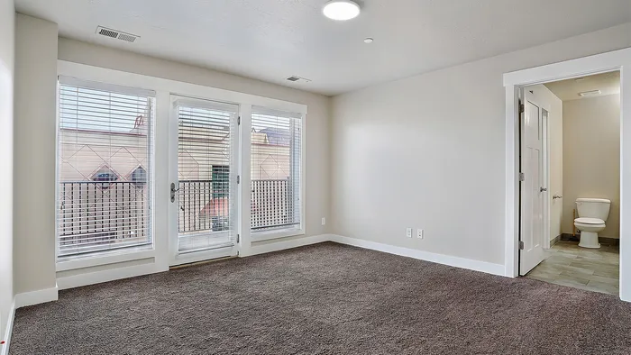 Bedroom at Junction View Apartments with large windows, balcony access, and private bathroom entry.