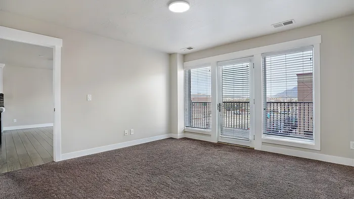 Spacious bedroom at Junction View Apartments with large windows, balcony access, and natural light in Ogden, Utah.