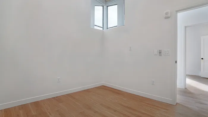 Second bedroom with high window and wood flooring in a Greenside penthouse