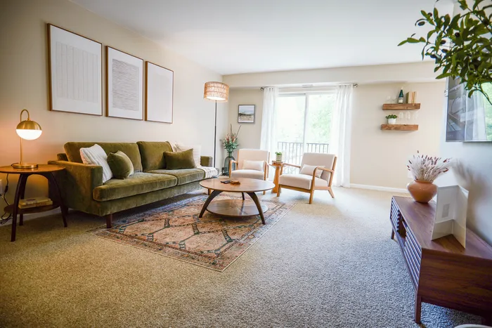 Inviting living room with warm, natural light, featuring a plush green sofa, modern armchairs, and elegant decor for a cozy ambiance.