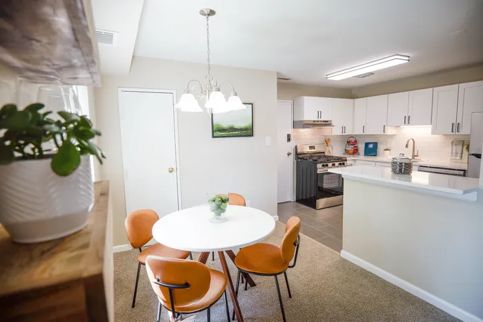 Bright and inviting kitchen and dining area featuring a modern design with white cabinets, sleek appliances, and a stylish round dining table set with warm-toned chairs.