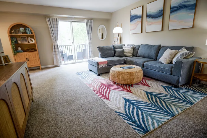 Bright living room with a cozy gray sectional, colorful area rug, and elegant decor opening to a balcony view.
