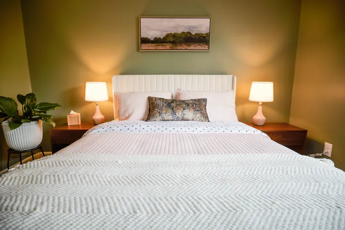 Charming bedroom with cozy bedding, elegant green walls, and warm lighting, offering a serene retreat.