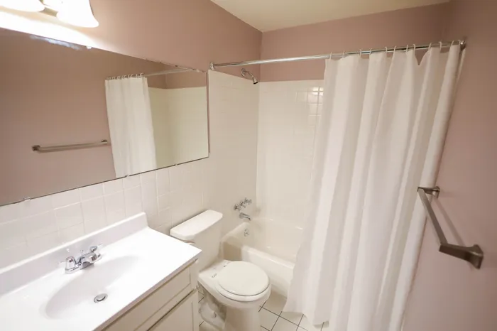 Modern bathroom with elegant white fixtures, spacious mirror, and soft pink walls.