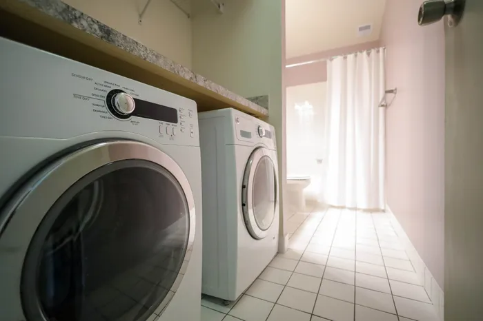 Modern laundry area with sleek washing machine and dryer adjacent to a bright, tiled bathroom.