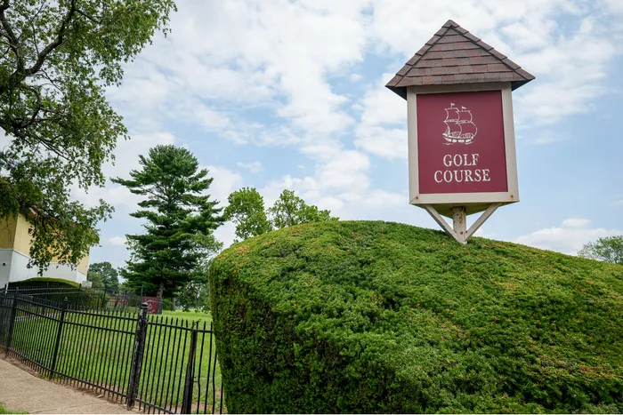 Lush green landscape with a charming golf course sign, bordered by vibrant foliage under a clear blue sky.